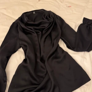 Svart blus från Niay - Elegant svart blus från Niay med långa ärmar och en draperad krage. Perfekt för en stilren look. Tillverkad i ett mjukt och följsamt material som ger en lyxig känsla.