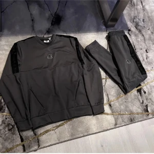 Grå sweatshirt och byxor från Adidas - Säljer ett set med grå sweatshirt och matchande byxor från Adidas. Tröjan har långa ärmar och ett diskret logotyptryck på bröstet. Byxorna har en elastisk midja med dragsko och logotyp på benet. Perfekt för en avslappnad stil. Vid frågor hör av er.