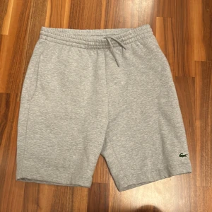 Grå shorts från Lacoste - Snygga grå shorts från Lacoste med elastisk midja och snörning. Perfekta för en avslappnad stil. Den klassiska krokodilloggan ger en sportig touch.