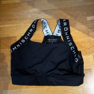 Svart sporttopp från Röhnisch - Säljer en svart sporttopp från Röhnisch med breda axelband som har logotypen i vitt. Toppen är perfekt för träning och har en bekväm passform.