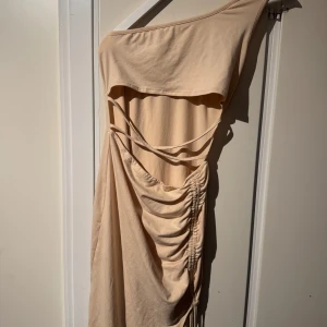 Beige oneshoulder klänning - Snygg beige oneshoulder klänning med draperad design och knytning i sidan. 