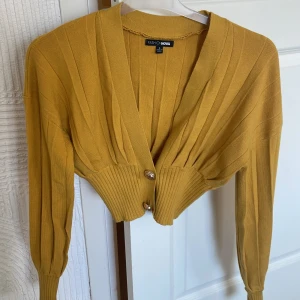 Fashionnova kofta - Croppad stickad senapsgul kofta med guldknappar. Använd fåtal gånger, mest hängt i garderoben. 