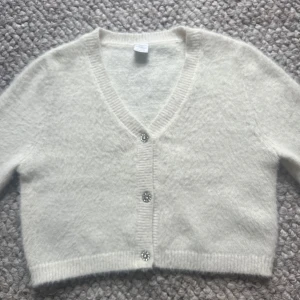 Vit kofta från Lindex - Säljer en söt vit kofta från Lindex i storlek 146/152. Koftan har en  v-ringning  med glittriga knappar framtill. Den är mjuk och bekväm!💕