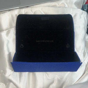 Blått glasögonfodral - Snyggt och praktiskt glasögonfodral i en djup blå färg. Fodralet är tillverkat av återvunnet material och har en stilren design. Perfekt för att skydda dina glasögon när du är på språng.