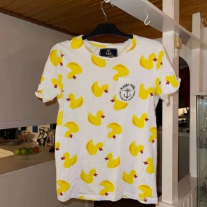 Vit t-shirt med gula ankor från Blount & Pool - Säljer en cool vit t-shirt från Blount & Pool med ett lekfullt mönster av gula ankor. T-shirten är kortärmad och tillverkad i ekologisk bomull. Perfekt för en avslappnad stil med en unik touch!