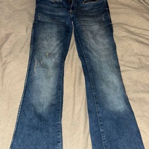 Blå bootcut jeans från H&M - Säljer ett par blå bootcut jeans från H&M med justerbar midja. De har en låg midja och klassisk femficksdesign. Perfekta för en avslappnad stil.