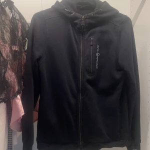 Svart zip hoodie från Sail Racing - Snygg svart zip hoodie från Sail Racing med dragkedja och huva. Jackan har en bröstficka med dragkedja och luva. Mycket bra sick. Pris kan diskuteras❤️