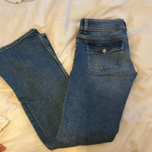 Blå bootcut jeans med knapp fickor där bak - Snygga blå jeans med bootcut och låg midja. Dem har knapp fickor där bak och dubbla knappar i midjan. Gina Young