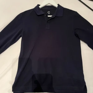 Mörkblå pikétröja - Säljer en stilren mörkblå pikétröja med klassisk krage och knappar framtill. Passade mig när jag var 160 så skulle nog säga att den Passar en som är mellan 155-160 