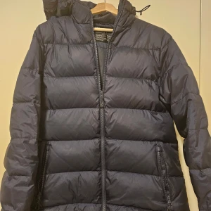 dunjacka från Neomondo - Säljer en dunjacka från Neomondo med dragkedja och huva. Jackan är perfekt för kalla dagar och har en stilren design med quiltade paneler. Den är utrustad med praktiska fickor med dragkedjor.