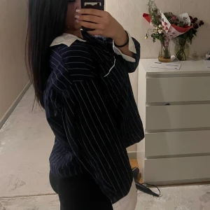 Svartvit randig skjorta - Snygg marinblå skjorta med vita ränder och kontrasterande vita manschetter och krage. Skjortan har en avslappnad passform och knappar framtill. Perfekt för en stilren look.