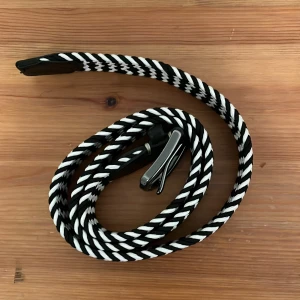 Svartvitt flätat bälte - Snyggt svartvitt flätat bälte med ett unikt mönster. Bältet har en stilren metallspänne i silverfärg som ger en modern touch. Perfekt för att ge din outfit en extra detalj.