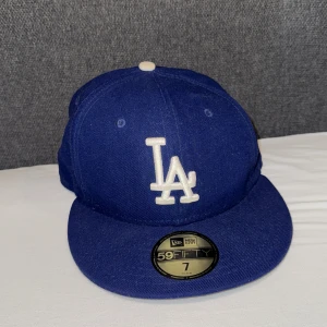 Blå keps från New Era LA - Snygg blå keps från New Era med LA-logga framtill. Klassisk 59FIFTY-modell med platt skärm och broderad MLB-logga baktill. Perfekt för att komplettera din streetwear-look. Storlek 7