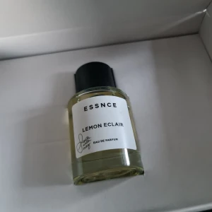 Essnce Lemon Eclair Eau de Parfum - Fräsch och livlig doft av citron i en stilren flaska. Essnce Lemon Eclair Eau de Parfum kommer i en genomskinlig glasflaska med svart lock och vit etikett. Perfekt för den som älskar citrusdofter.