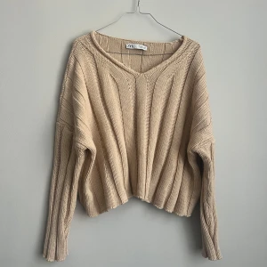 Beige stickad tröja från Zara - Säljer en snygg beige stickad tröja från Zara. Tröjan har en v-ringad design och långa ärmar, perfekt för kyligare dagar. Den har en lös passform som ger en avslappnad look. Perfekt att matcha med jeans eller kjol för en stilren outfit.