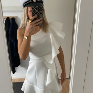 Vit oneshoulder klänning - Snygg vit oneshoulder klänning med volangdetaljer. Perfekt för sommarens festligheter. Den har en kort längd och en elegant passform, passar perfekt till studenten och midsommar😍