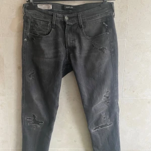 Svarta jeans från Replay - Snygga svarta jeans från Replay med slitna detaljer för en cool look. De har en super slim fit och är perfekta för en trendig stil. Midjan är märkt som storlek 29.