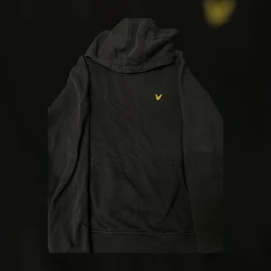 Svart hoodie från Lyle & Scott - Säljer en stilren svart hoodie från Lyle & Scott med deras ikoniska logga på bröstet. Tröjan har en klassisk känguruficka och en bekväm huva med dragsko. Perfekt för en avslappnad stil. Köpte den för 849kr från zalando.