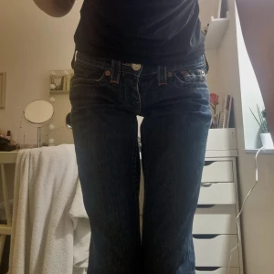 Blå jeans från True Religion w24 - Snygga blå jeans från True Religion med klassisk femficksdesign och kontrastsömmar. De har en låg midja och en knappgylf med märkets logga. Perfekta för en avslappnad stil. Ej bootcut modell, storlek w24