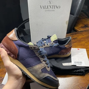 Valentino Rockrunner  - Exklusiva Valentino Garavani Rockrunner sneakers i ett snyggt camouflage-mönster! En perfekt kombination av lyx och streetwear, med premiumkvalitet och de ikoniska nitarna vid hälen. |  Färg: Camouflage (Brun, röd, blå) 🤎❤️💙 | Material: Mix av mocka och läder 🏆| Skick: Använda🙌 | Storlek: 41 👌| Box: Originalbox, Dustbag och kvitto 📦✨ | 🚚 Leverans: Skickas snabbt via PostNord eller instabox | 💬 Skicka ett meddelande vid frågor!