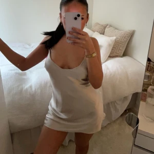 Champagnefärgad axelbandslös klänning - Säljer en elegant champagnefärgad axelbandslös klänning. Perfekt för en stilren look med sin släta design och korta längd. Klänningen har en figurnära passform som framhäver silhuetten.