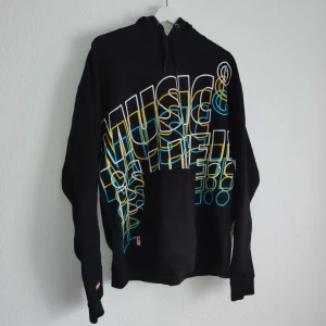 Svart hoodie från Nesta - Säljer en svart hoodie från Nesta med färgglatt tryck 'Music is Life' i blått och gult. Tröjan har långa ärmar och en bekväm passform. Perfekt för musikälskare! 🎶