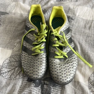 Adidas AG Elite  - Snygga fotbollsskor från Adidas i grått med neongula detaljer och snörning. Skorna har ett geometriskt mönster och tre svarta ränder på sidan. Perfekta för fotbollsplanen! Behöver underlag. 