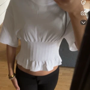 Figursydd vit topp - Aldrig använd, finns prislapp!! Säljer en vit ribbad topp med korta ärmar och volangdetalj vid nederkanten. Toppen har en tight passform som framhäver. 