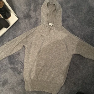 Grå Kashmir hoodie från Carmés - Säljer en stilren grå hoodie från Carmés i storlek S. Tröjan har en klassisk design med huva och långa ärmar, perfekt för en avslappnad look. Den är tillverkad i ett mjukt material Kashmir  som ger en bekväm känsla.