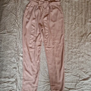 Rosa byxor från BikBok - Snygga rosa byxor från BikBok med hög midja och knytband. Byxorna har en loose passform och är perfekta för en avslappnad stil. De har fickor på sidorna och är tillverkade i ett mjukt material som ger en bekväm känsla. Liten fläck framtill se bild