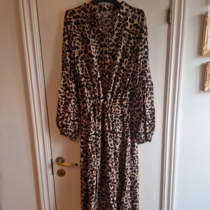 Leopardmönstrad klänning - Snygg leopardmönstrad klänning med långa ärmar och knappar framtill. Perfekt för att sticka ut med stil. Klänningen har en bekväm passform och är gjord i ett lätt material.