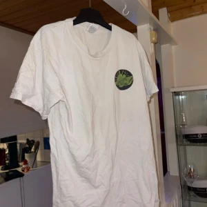 Vit t-shirt med grönt tryck - Säljer en vit t-shirt med ett coolt grönt tryck på framsidan. Trycket föreställer en bil och texten 'Smoke EM' med olika symboler runtomkring. Perfekt för en avslappnad stil.