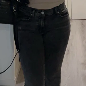 Svart/grå jeansbyxor - Snygga svarta jeansbyxor med en klassisk design. De har en normal passform och är perfekta för en stilren look. Byxorna har knappar och dragkedja framtill.