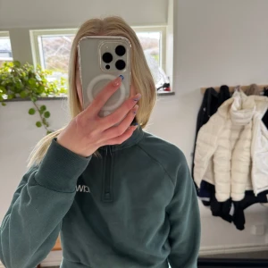 Mörkgrön tröja med dragkedja från ICANIWILL - Säljer en mörkgrön tröja från ICANIWILL med halv dragkedja och hög krage. Tröjan har långa ärmar och ribbade muddar vid ärmslut och nederkant, tröjan är ganska kort men otroligt skön. Perfekt att använda som en träningströja eller som en mys tröja. Nästan aldrig använd.