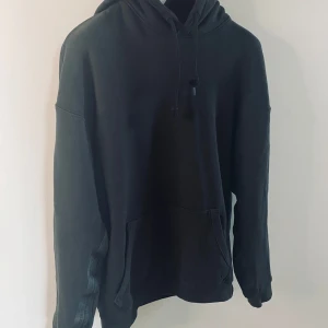 Nyskick svart hoodie från Adidas - Svart hoodie med snygga, diskreta detaljer från Adidas i klassisk design.. Den har en justerbar huva med dragsko och Adidas-logga längs sidan. 