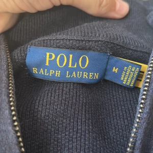 Mörkblå tröja från Polo Ralph Lauren - Säljer en stilren mörkblå tröja från Polo Ralph Lauren. Tröjan har en dragkedja vid halsen och är tillverkad i ett mjukt material. Perfekt för en avslappnad och snygg look. Den kostar 2100kr helt ny och den här är max använd 10 ggr. Pris kan diskuteras!