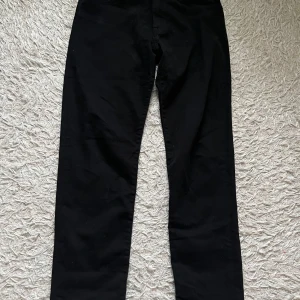 Svarta byxor från BOSS - Snygga svarta byxor från BOSS med en klassisk design. Byxorna har en normal passform och är perfekta för en stilren look. Tillverkade i ett bekvämt material med subtila detaljer som ger en exklusiv känsla. Byxorna kostade 1189 kr och har använts 3 gånger.