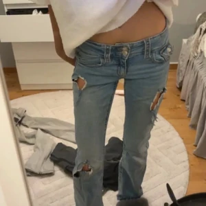 Blå jeans med slitningar - Snygga blå jeans med slitningar på knäna och låren. De har en klassisk femficksdesign och en knappgylf. Perfekta för en avslappnad stil.