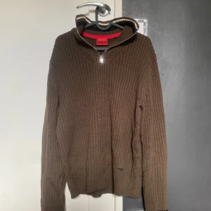 stickad halfzip från Hugo boss - Säljer en brun stickad tröja från Hugo boss med dragkedja vid halsen. Tröjan har långa ärmar och en ribbad struktur som ger en stilren look. Perfekt för kyligare dagar. Jag säljer tröjan då jag knappast använder den.