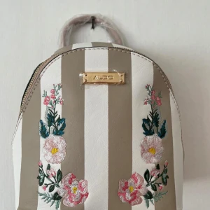 Aldo väska  - Ljusrosa ryggsäckväska från amerikanska märket Aldo. Aldrig använd, helt ny! Justerbar så man kan ha den som ryckande eller väska som hänger på sidan. Köpt den Miami för 600kr, men säljer den nu för 399kr.💕 blommorna är broderade på dig lädret:)