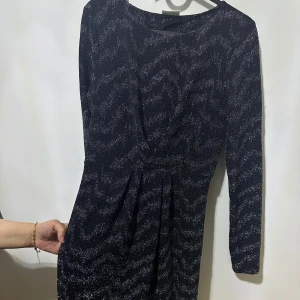 Svart glittrig klänning - Snygg svart klänning med glittrigt mönster. Den har en figurnära passform och långa ärmar, perfekt för en kväll ute. Klänningen är kort och har en elegant design som drar blickarna till sig.