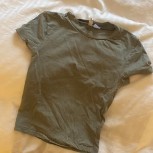 Olivgrön t-shirt från H&M - Säljer en olivgrön t-shirt från H&M Divided. Den har en enkel design med korta ärmar och rund hals. Den är även lite magtröja. Kontakta innan köp eller vid frågor😊