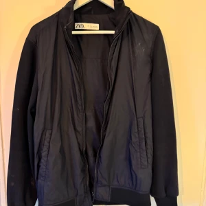 Svart jacka från Zara - Säljer en stilren svart jacka från Zara med dragkedja framtill. Jackan har långa ärmar och ribbade muddar vid ärmslut och nederkant. Perfekt för en casual look. Storlek M