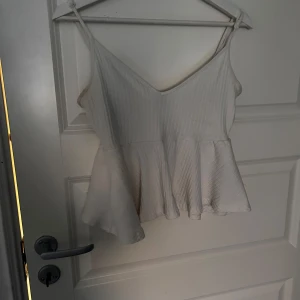 Vit ribbad linnetopp från Shein - Säljer en vit ribbad linnetopp från Shein. Toppen har smala axelband och en lätt utsvängd nederdel som ger en fin siluett. Perfekt för varma dagar eller som ett lager under en jacka.