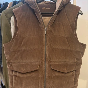 Brun manchester dunväst från Stenströms - Snygg brun manchester dunväst från Stenströms med dragkedja och praktiska fickor framtill. Perfekt för kyligare dagar med sin quiltade design och huva. Ett stilrent val för den modemedvetna.