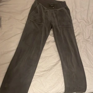 Grå mjukisbyxor från Juicy Couture - Snygga grå mjukisbyxor från Juicy Couture med bred resår i midjan och praktiska fickor både fram och bak. Perfekta för en avslappnad stil med en touch av lyx. Byxorna har en loose passform och är tillverkade i ett mjukt material som känns skönt mot huden.