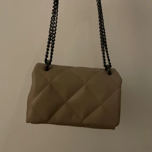 Beige quiltad miniväska - Snygg miniväska med quiltat mönster och kedjehandtag. Från behärska och är helt ny det vill säga aldrig använd 