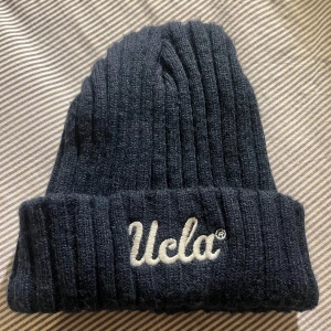 mörkblå ribbad mössa från Pull&Bear - Snygg mörkblå ribbad mössa från Pull&Bear med broderad text 'Ucla' framtill. Perfekt för kyliga dagar och ger en stilren look. Tillverkad i ett mjukt och bekvämt material.