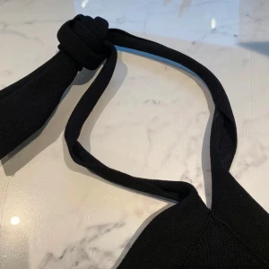 Svart ribbad halterneck topp - Snygg svart ribbad halterneck topp med knytband i nacken. Perfekt för en stilren look. Toppen är ärmlös och har en tight passform.