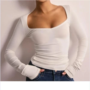 Vit långärmad topp med spetsdetalj - Snygg vit långärmad topp med en fin spetsdetalj längs den fyrkantiga halsringningen. Toppen har en tight passform och är perfekt för en stilren look. Tillverkad i ett mjukt och stretchigt material för extra komfort.pris kan diskuteras 